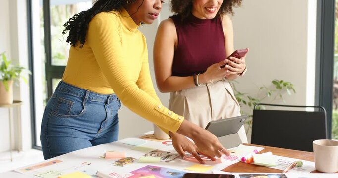 Seeing mockups, diverse female coworkers arranging layouts finalizing design on table in office