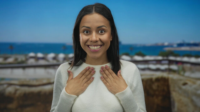 Woman celebrating feeling ecstatic with hands on face outdoors against a beautiful beach landscape showing pure joy and surprise.