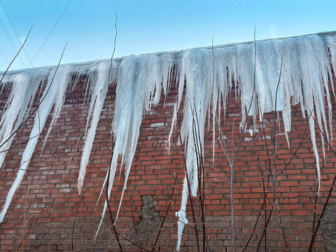 Large icicles hang from the roof of the building. Blue sky close up winter photo