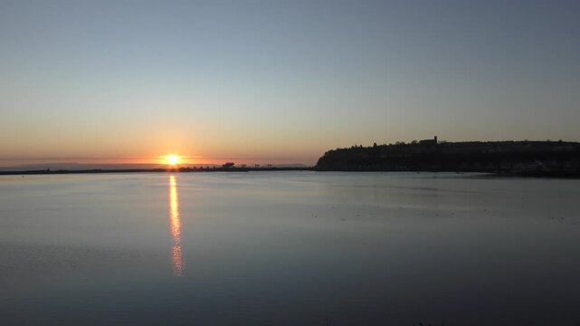 Calm Morning Sunrise over Cardiff Bay showing still water and the Barrage. Sun just above horizon and showing cliff at Penarth.