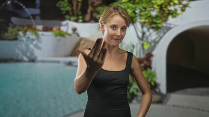 Woman speaking and showing open hand stop gesture at a poolside building in a black tank top, palm forward; assertion instruction.