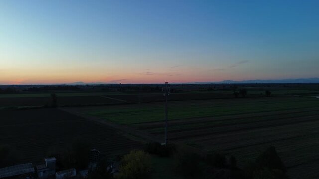 Professional twilight shot of a telecommunications tower in the Italian Po Valley, featuring a vibrant sunset horizon and expansive agricultural fields.