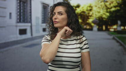 Fototapeta premium Young hispanic woman with bare hand makes throat slit gesture on busy city street in daylight; threat.