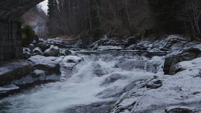 River flowing under a brigde with a strong current flowing down the valley and through the woods in Norway