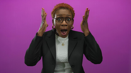 Young african american woman wearing glasses raising hands near face in surprised gesture in studio...