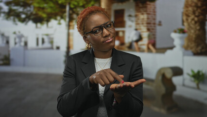 Young african american woman points finger to her open palm on street; money request urgent plea.