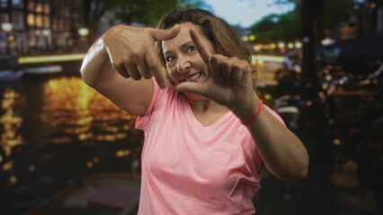 Woman frames canal water with hands on street; creative vision joy.