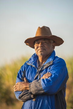 Portrait of elderly farm worker wearing winter coat and cowboy hat, with his arms crossed, looking at the camera while standing in field.