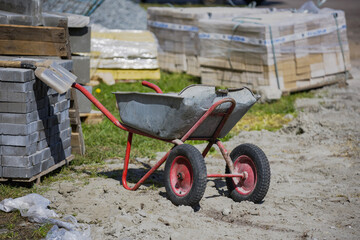 A wheelbarrow sits beside piles of bricks and stones on a construction site during a sunny...