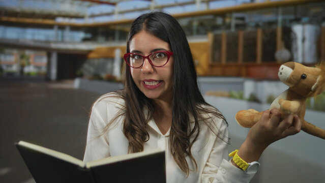 Woman reading aloud holding a lion puppet, outdoors with glasses, showcasing storytelling on a sunny street.