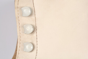A macro view of white leather on a figure skate showing the detailed texture of the material and three metal lace hooks with stitching