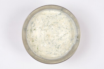 A top down view of a creamy white sauce or dip made with sour cream mixed with freshly chopped green dill and minced garlic in a metal bowl