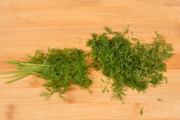 A top down view of fresh green dill branches and finely chopped herb spread across a textured wooden cutting board surface