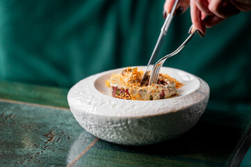 A close-up shot of a person using modern cutlery (tweezers and a fork) to eat a gourmet dish,...
