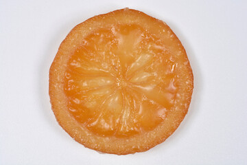 A top down view of a single round slice of sweet candied orange with a glistening sugar coating isolated on a plain white surface