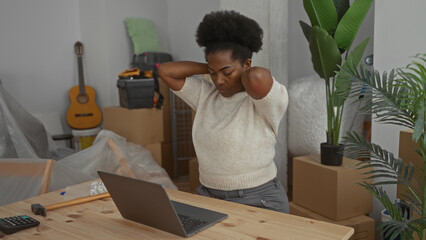 Young woman stretches at desk in new apartment surrounded by boxes and plants showing everyday life...