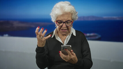 Senior woman holding lit smartphone, raised hand gesture and open mouth on white seaside terrace with cruise ship visible; frustration tech problem.