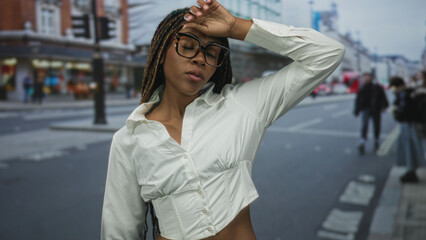 Obraz premium African american woman wearing glasses and white blouse touching forehead and smiling while standing on a busy city street; confidence independence boldness.
