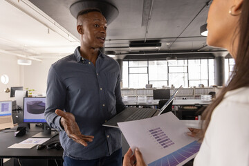 Diverse coworkers analyzing bar graph data with laptop, charts in open plan office