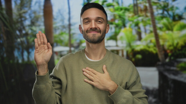 Young hispanic man outdoors in green park making pledge gesture with trees background exuding confidence and sincerity under bright natural light wearing casual outfit and smiling slightly