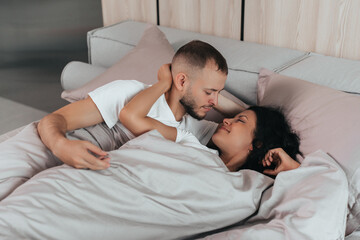A couple lays comfortably in bed, gazing into each other's eyes, wrapped in soft blankets.