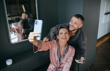 Couple sitting on the bed in robes, with the woman holding a snack and playfully engaging her partner, highlighting a light and easygoing atmosphere.