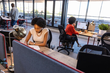 Diverse coworkers writing and viewing charts in office using notepad, computer and smartphone