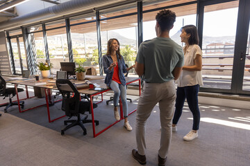 Diverse coworkers collaborating at red-framed desk in office using laptops