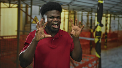 Man with hands clawed and grimacing inside a building construction site wearing a red polo shirt and showing bare fingers and hands; playful energy.
