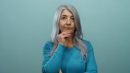 Senior woman with grey hair makes time out gesture against blue background conveying pause and contemplation in a thoughtful and expressive manner isolated from surroundings
