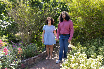 Diverse couple walking hand in hand along brick path through lush garden, flowering plants