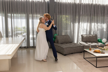 Bride and groom dancing in modern reception space with sheer gray curtains, table, balloons