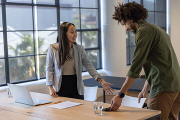 Diverse coworkers in business attire shaking hands at meeting table with laptop, tablet © wavebreak3