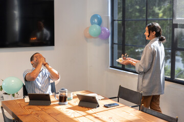 Diverse coworkers surprising colleague at office with cake, candles, pastel, balloons, copy space