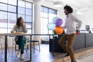 Diverse coworkers celebrating birthday surprise in work attire at office with gift, balloons