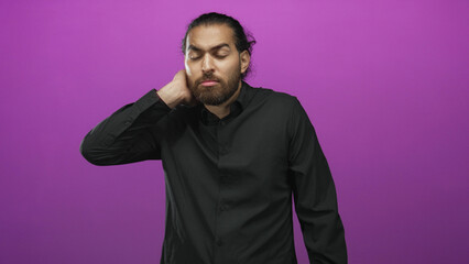Obraz premium Young bearded man touching neck with hand and wearing black shirt in purple studio; fatigue reflection introspection.