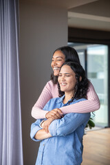 Asian women hugging in living room by sliding glass door with curtains, potted plant