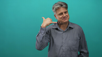 Man pointing finger and making call gesture with hand in studio teal backdrop; friendly confidence approachability.