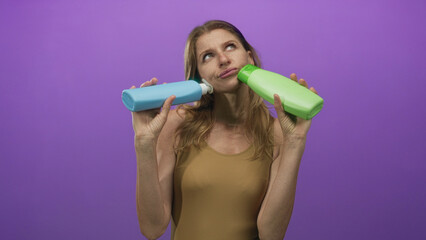 Woman holding two shampoo bottles while shrugging and comparing products in a purple studio backdrop; indecision choice comparison.