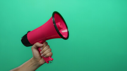 Hand holding pink megaphone against green background conveying communication and announcement concept.