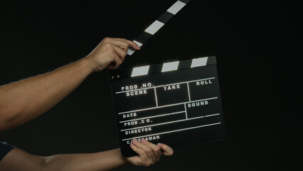 Obraz premium Man holding film clapperboard against black background signifies filmmaking and production process.