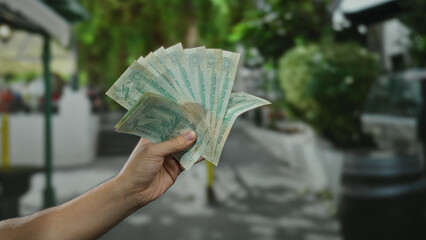 Man holding united arab emirates dirham banknotes in an outdoor city street setting, showcasing...