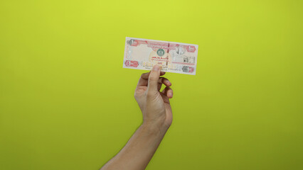 Male hand holding united arab emirates dirham banknote against a vibrant yellow background isolated sharply highlighting currency details and economic theme.