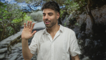 Young hispanic man points finger along a sunlit winding path in a green forest outdoors  welcome greeting. © Krakenimages.com