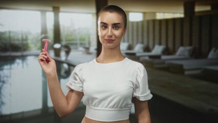 Woman with short buzz haircut holding pink razor aloft with bare forearm visible in building spa...