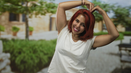 Woman making a heart shape with her hands and smiling in front of a sunlit stone building outdoors; joy friendship connection.
