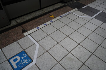 Waiting line sign and bicycle parking symbol on the floor of a subway platform.