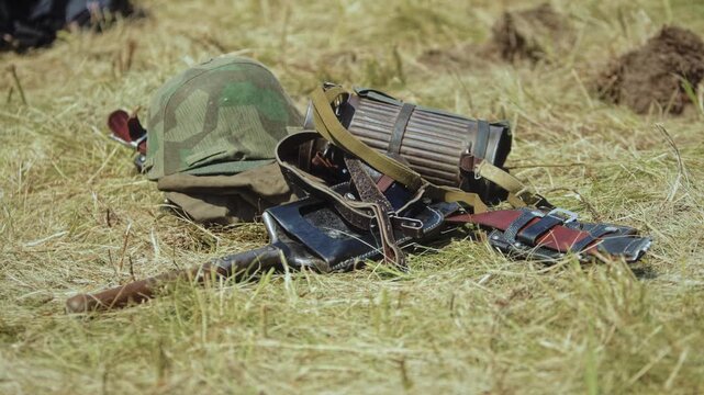 German Wehrmacht soldier gear on dry grass. Camouflage helmet, gas mask canister, entrenching tool in leather carrier rest on brown, green field. Historical World War 2 combat equipment