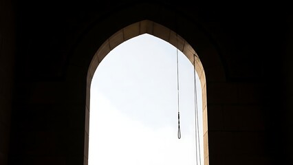 A light shines through an arched stone window with hanging chains arch architecture bright dark sky cloud interior detail
