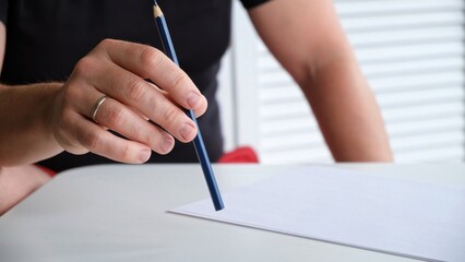 A man tapping a pen on a table with a blank sheet of paper. The concept of lack of ideas, problems,...